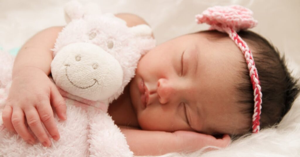 Adorable sleeping baby cuddling a plush toy, wearing a cute pink headband.
